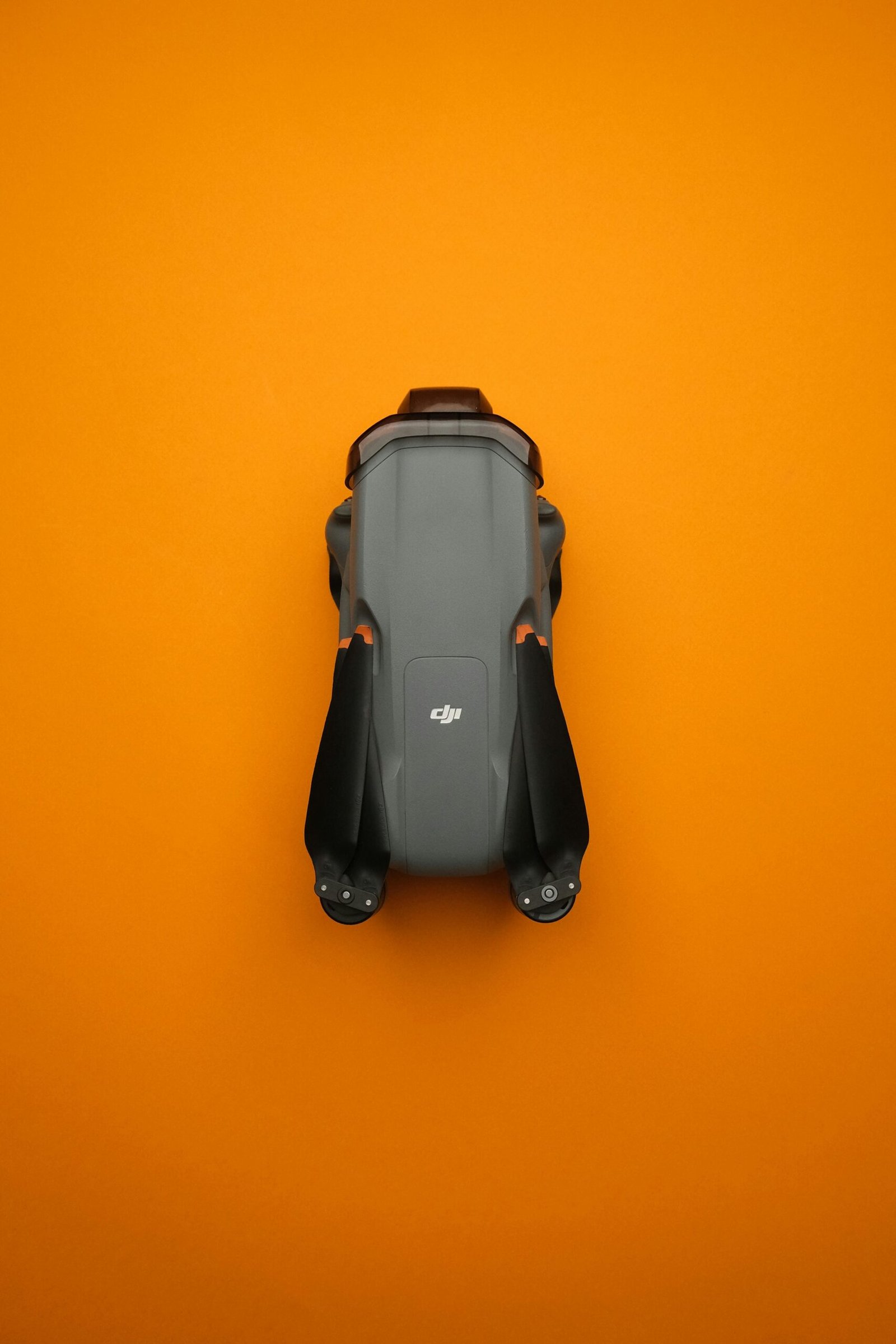 Top view of a compact gray drone, sharply contrasting with a vivid orange backdrop.